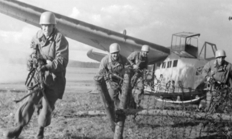 Black and white photo of 4 soldiers brandishing rifles on an airfield